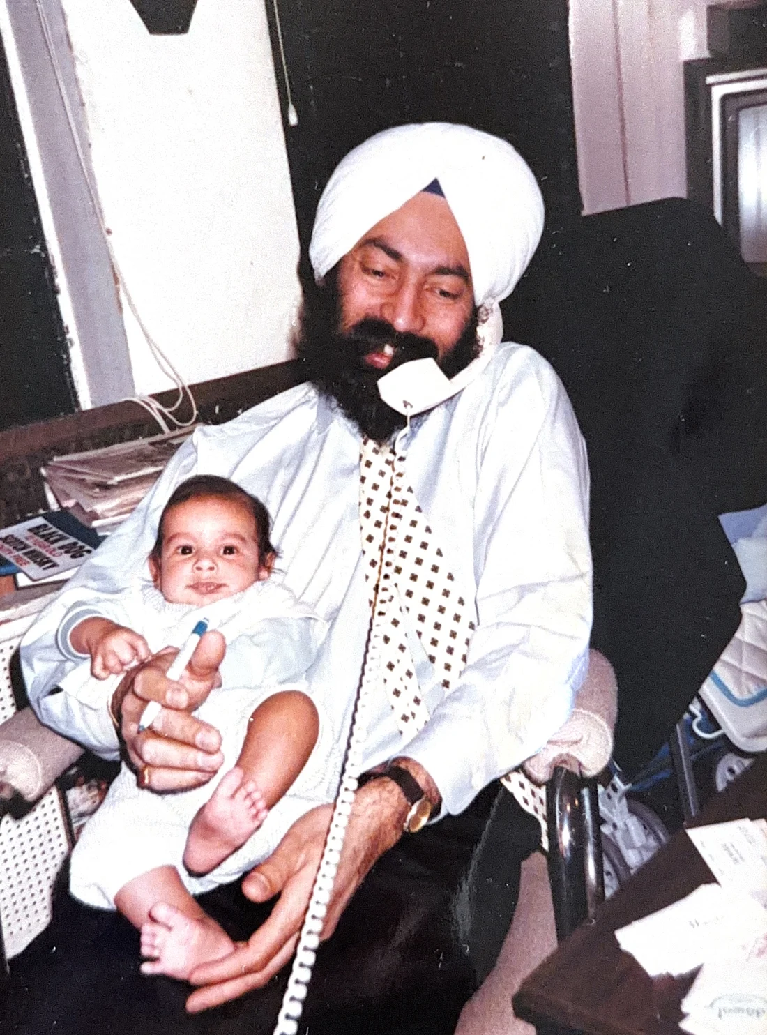 Tony Bedi at his desk, on the phone, holding his infant son Deep